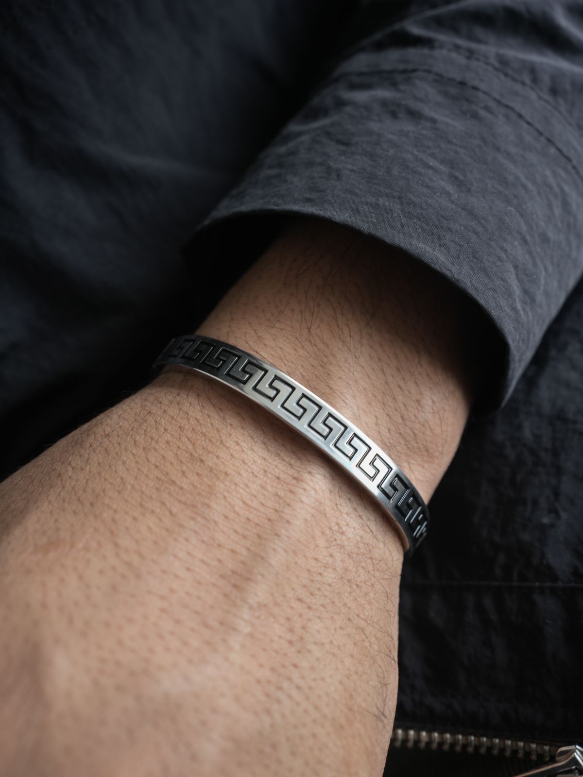 Silver bracelet with a geometric pattern on a wrist, wearing a dark jacket.